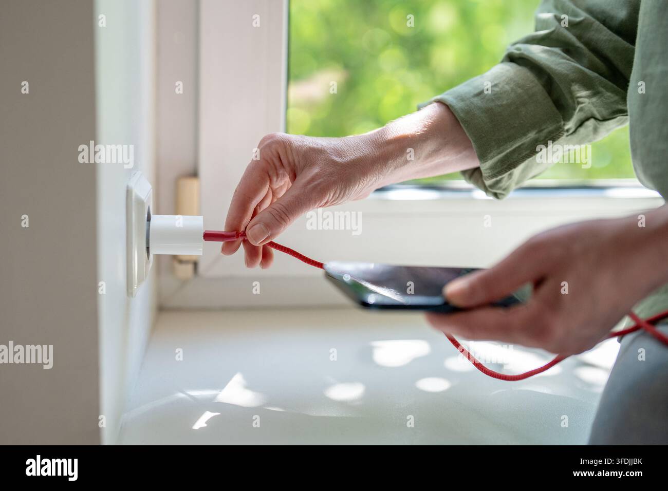 Donna piega un cavo USB difettoso vicino all'adattatore da parete per ripristinare la ricarica instabile dello smartphone a casa. Foto Stock