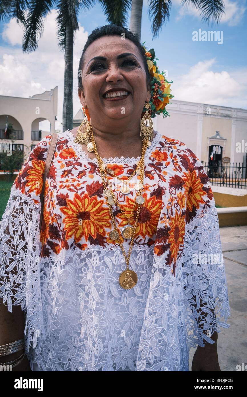 Valladolid, Messico - 01 ottobre 2024: Vista di una donna sorridente che indossa un tradizionale huipil bianco e arancione ricamato con maniche di pizzo e gioielli d'oro Foto Stock