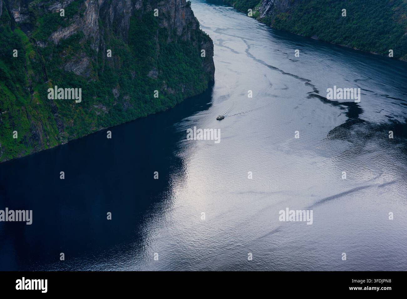 Prospettiva aerea di un profondo fiordo norvegese con alte scogliere rocciose, fitta vegetazione forestale e acqua che mostra modelli di correnti di marea. Foto Stock