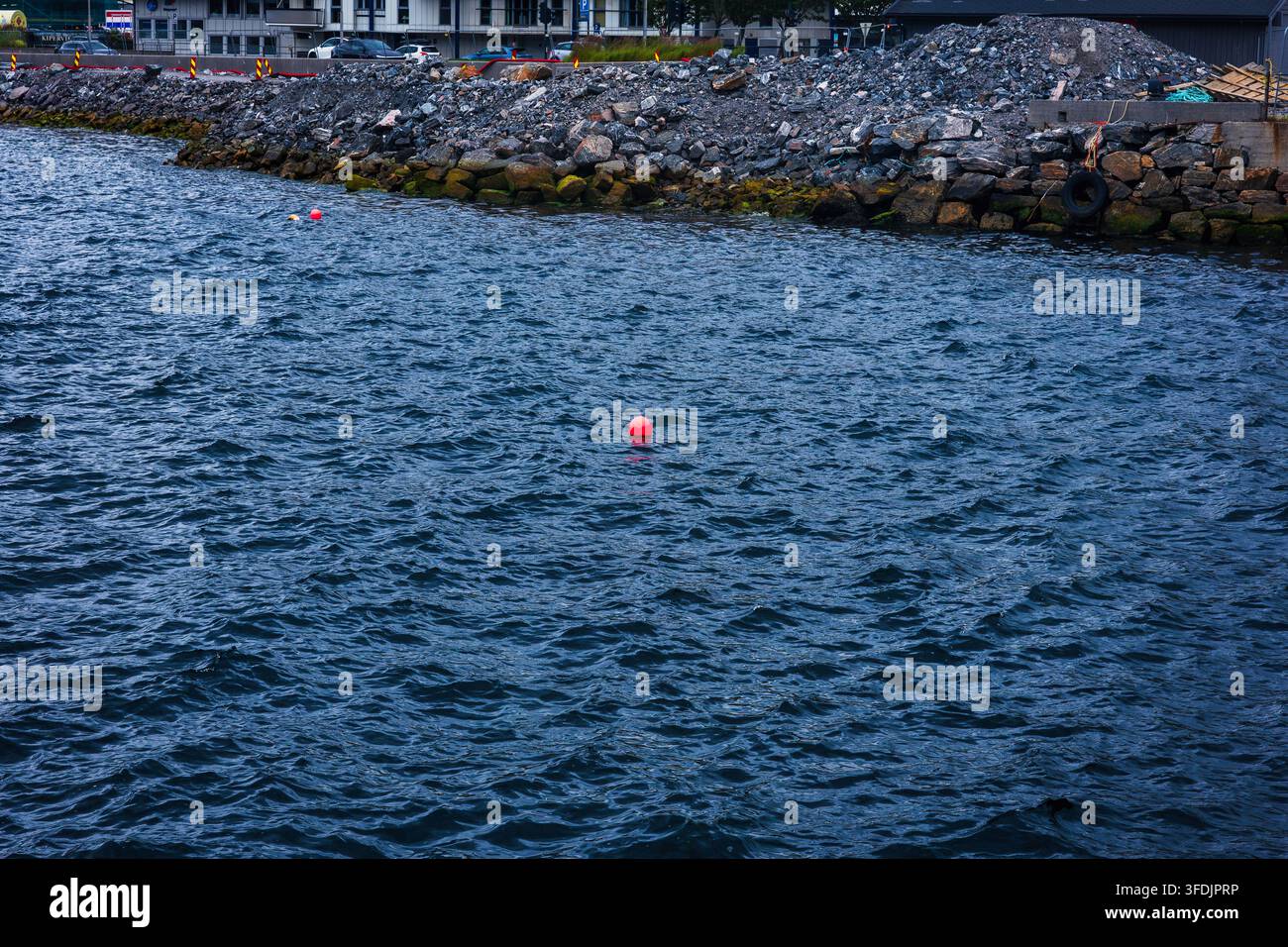 Boe rosse segnano l'area di nuoto vicino a un frangiflutti ricoperto di muschio. Impianto portuale industriale con barriere in pietra visibili sullo sfondo, Norvegia. Foto Stock
