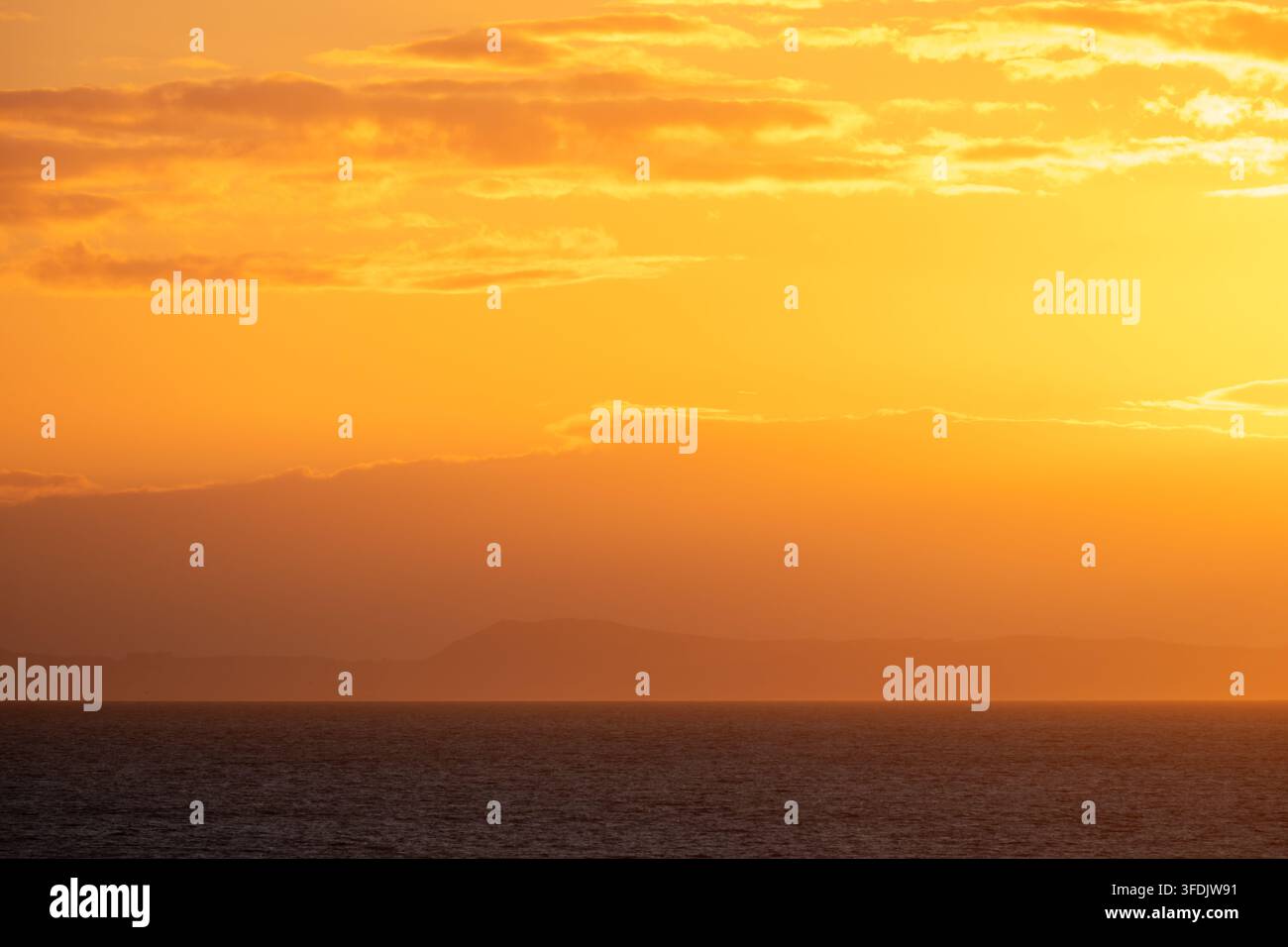 Tramonto rosso brillante sul mare con un'isola lontana all'orizzonte Foto Stock