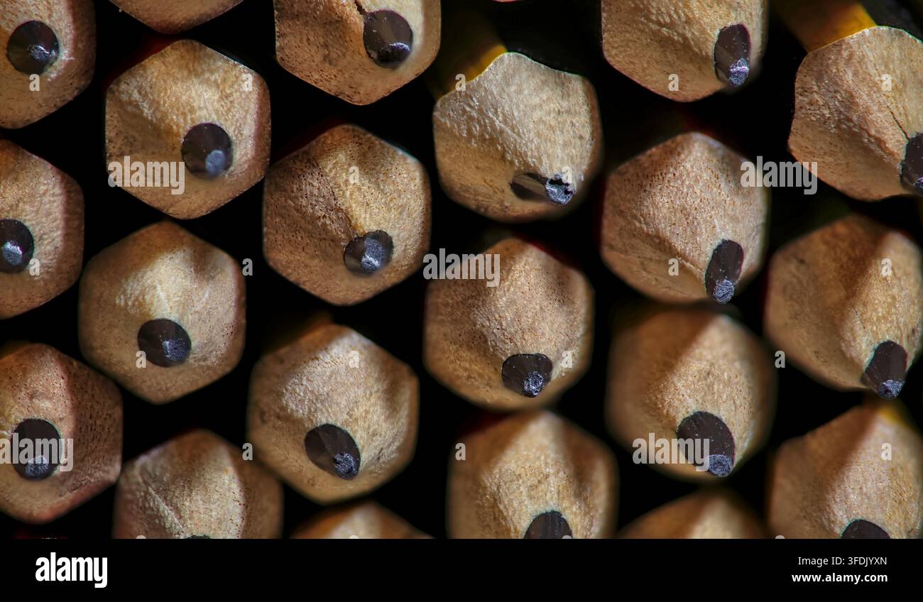 Macro primo piano di matite di grafite appuntite disposte in un modello ripetitivo su uno sfondo scuro. Foto Stock