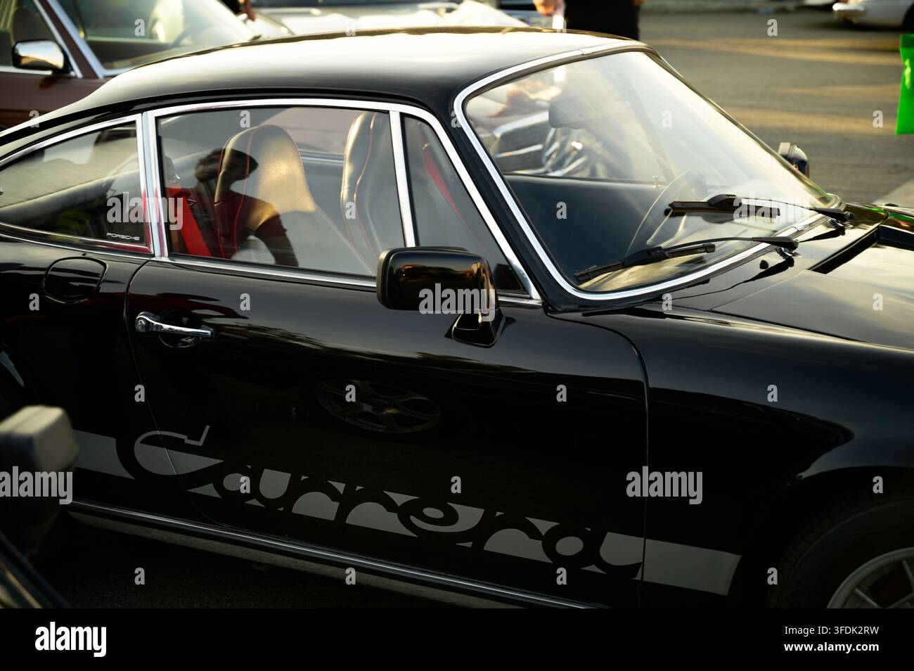 Uno scatto dettagliato di profilo laterale di una classica Porsche 911 Carrera nera, che evidenzia la sua silhouette iconica, il bordo cromato dei finestrini e i sedili da corsa vintage. Foto Stock
