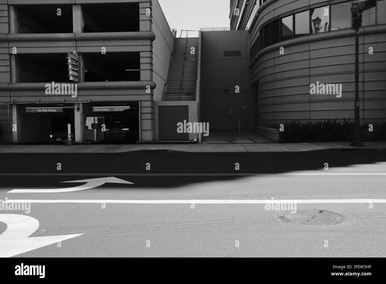 Edificio urbano moderno e struttura di parcheggio fotografati attraverso una strada del sud della California in bianco e nero. Foto Stock