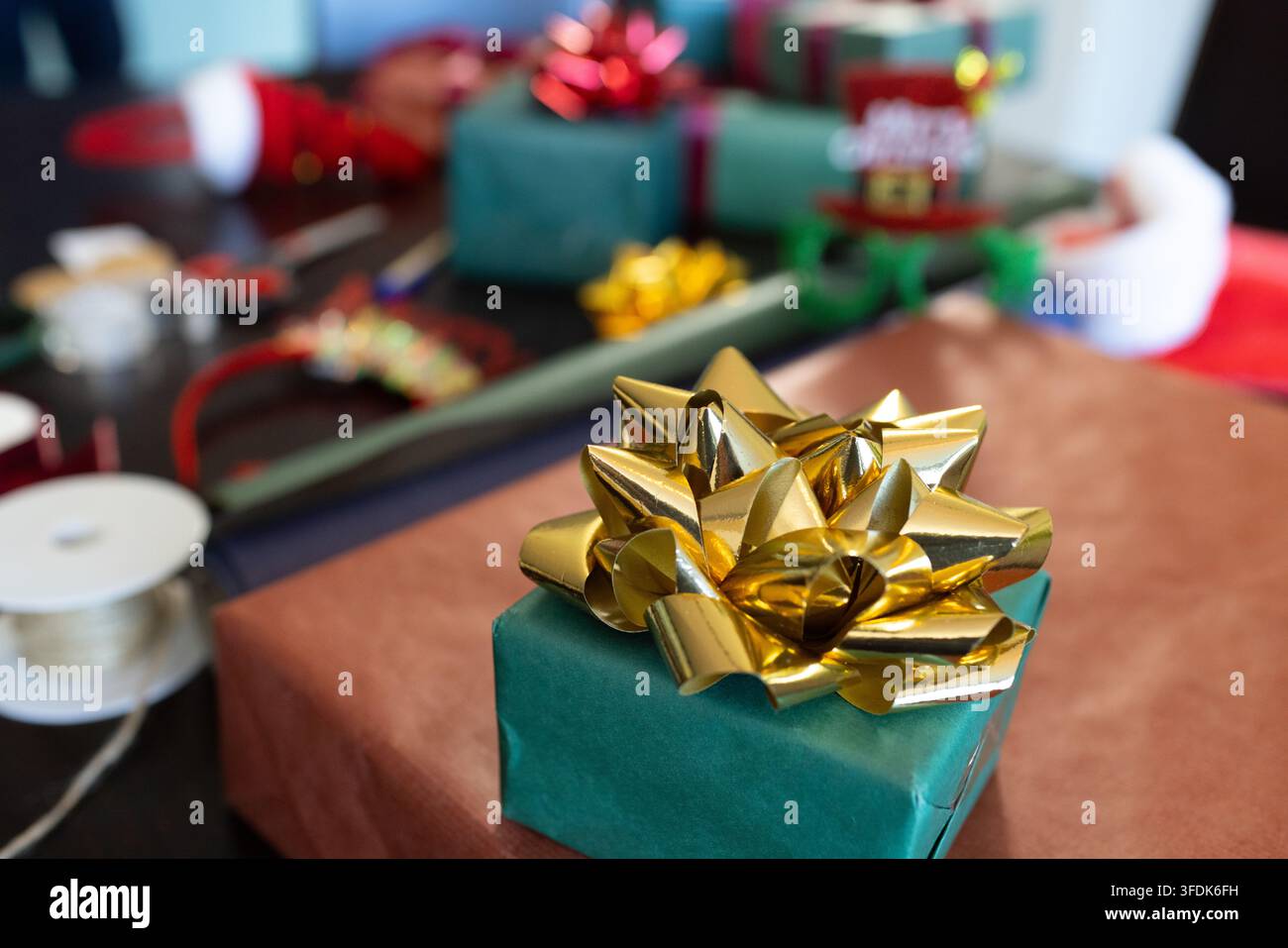 Piccola scatola regalo verde è posata su carta da regalo marrone sul tavolo, nastri natalizi la circondano Foto Stock