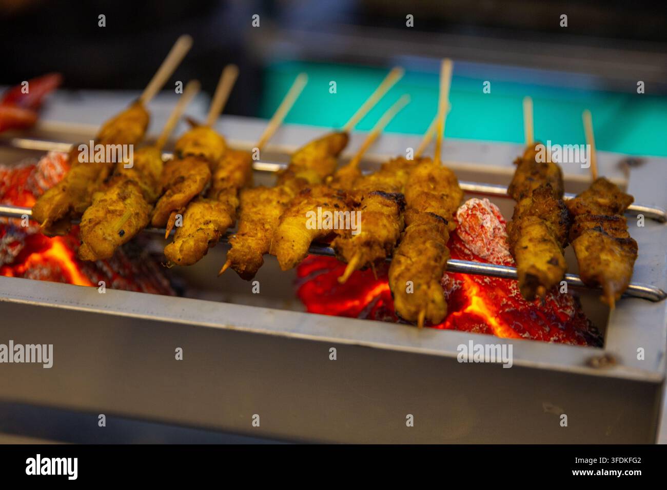 File di spiedini di satay di pollo stagionato che grigliano su carboni ardenti rossastri in una vasca metallica a uno stand del mercato notturno. Foto Stock