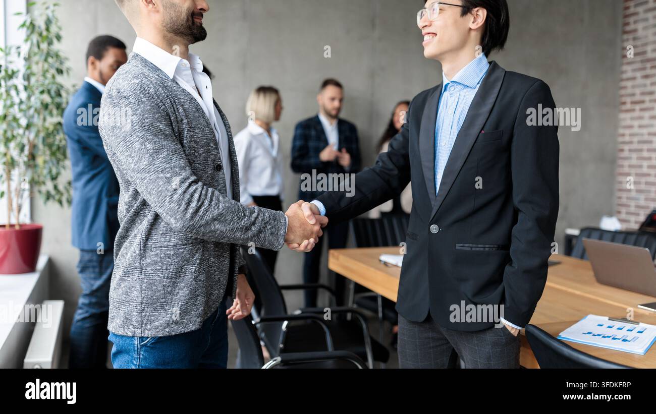 Due uomini d'affari che stringono la mano dopo aver negoziato con successo in ufficio Foto Stock