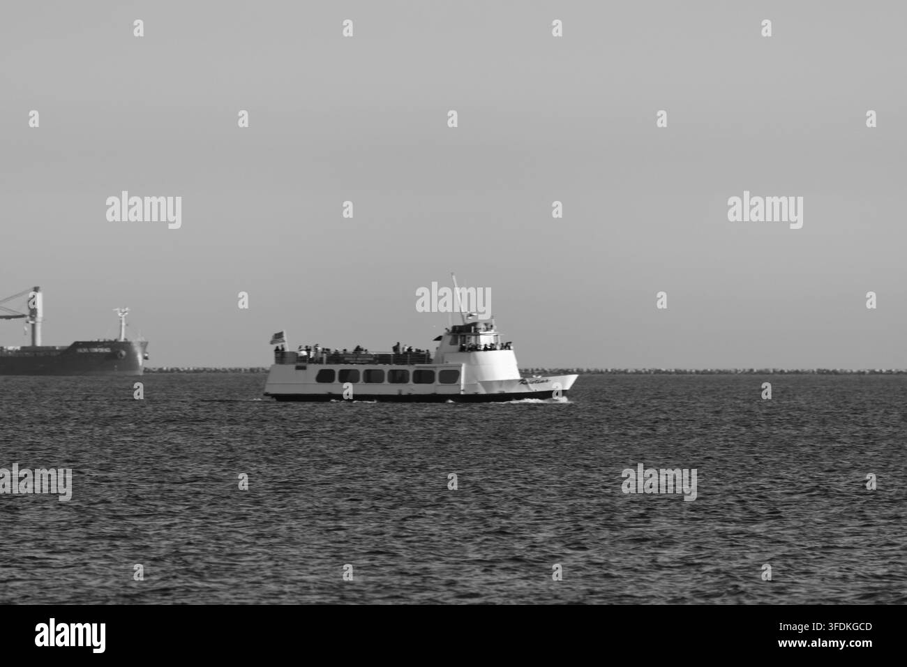Un battello passeggeri attraversa le acque aperte del porto vicino a una nave cargo lontana. Foto Stock