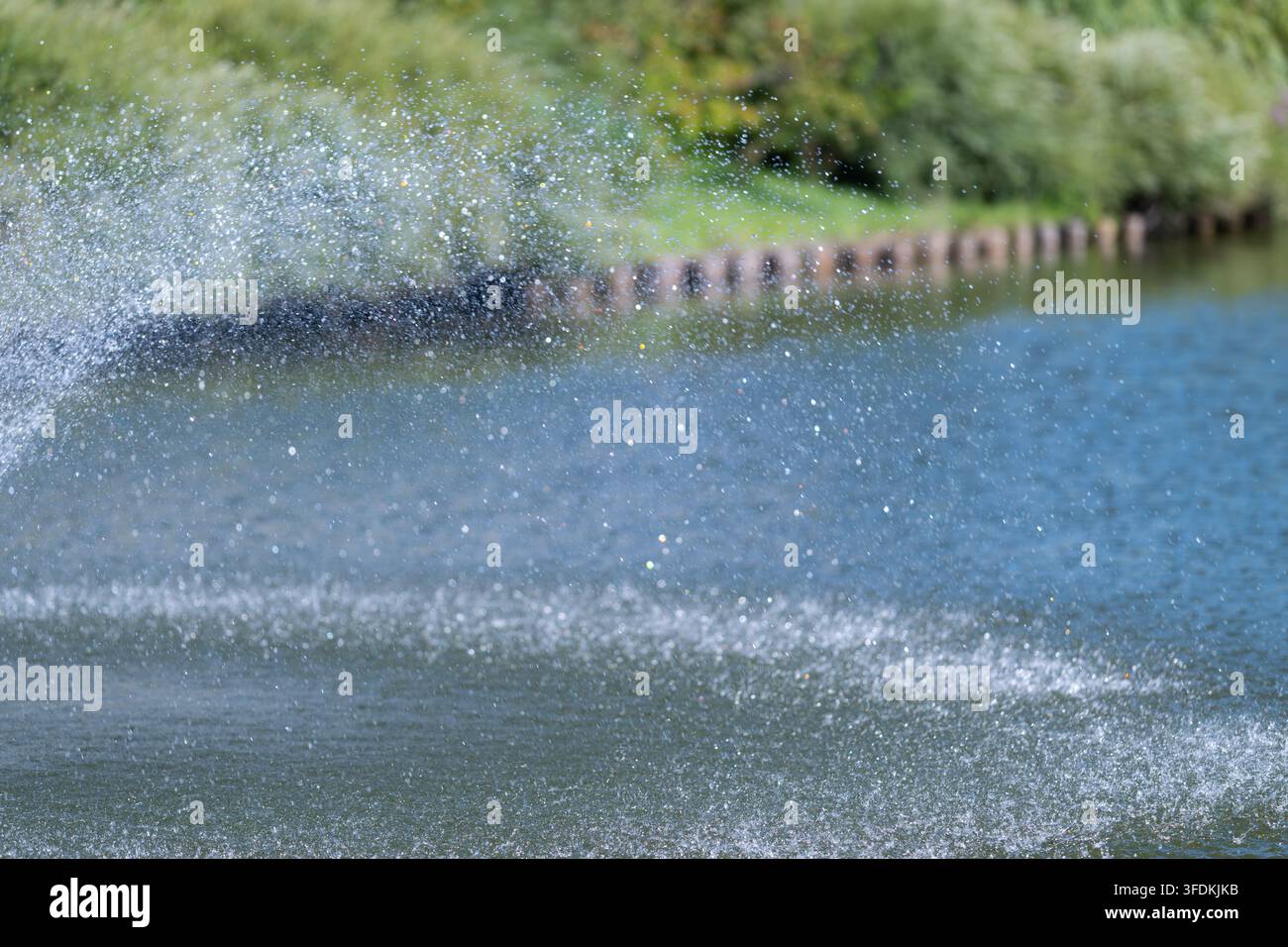 Vicino a un lago tranquillo, la luce del sole brilla sulla superficie mentre le goccioline d'acqua vengono lanciate in aria creando uno splendido spettacolo di lucentezza e gioia Foto Stock