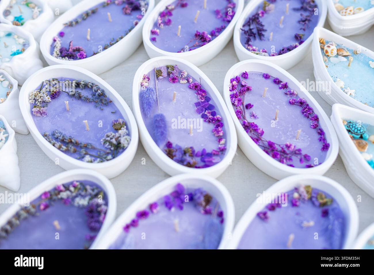 Candele floreali viola decorate con fiori secchi. Candele viola in contenitori bianchi ovali decorate con fiori secchi, petali, erbe e molteplici Foto Stock