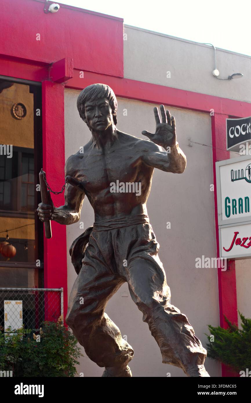 Statua di bronzo di Bruce Lee in posa dinamica di arti marziali. Scultura si trova all'aperto vicino a una facciata di edificio colorata. L'opera d'arte cattura il combattimento iconico di Lee Foto Stock