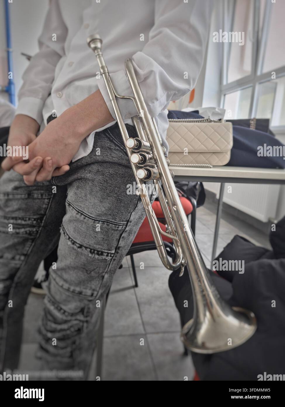 Primo piano di uno studente delle superiori in camicia bianca che tiene uno strumento a tromba in ottone argentato lucido Foto Stock