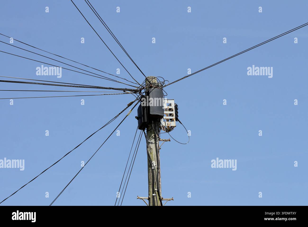 Un fascio di cavi d'acciaio irradia da un palo telegrafico nel sud dell'Inghilterra contro un cielo blu semplice Foto Stock