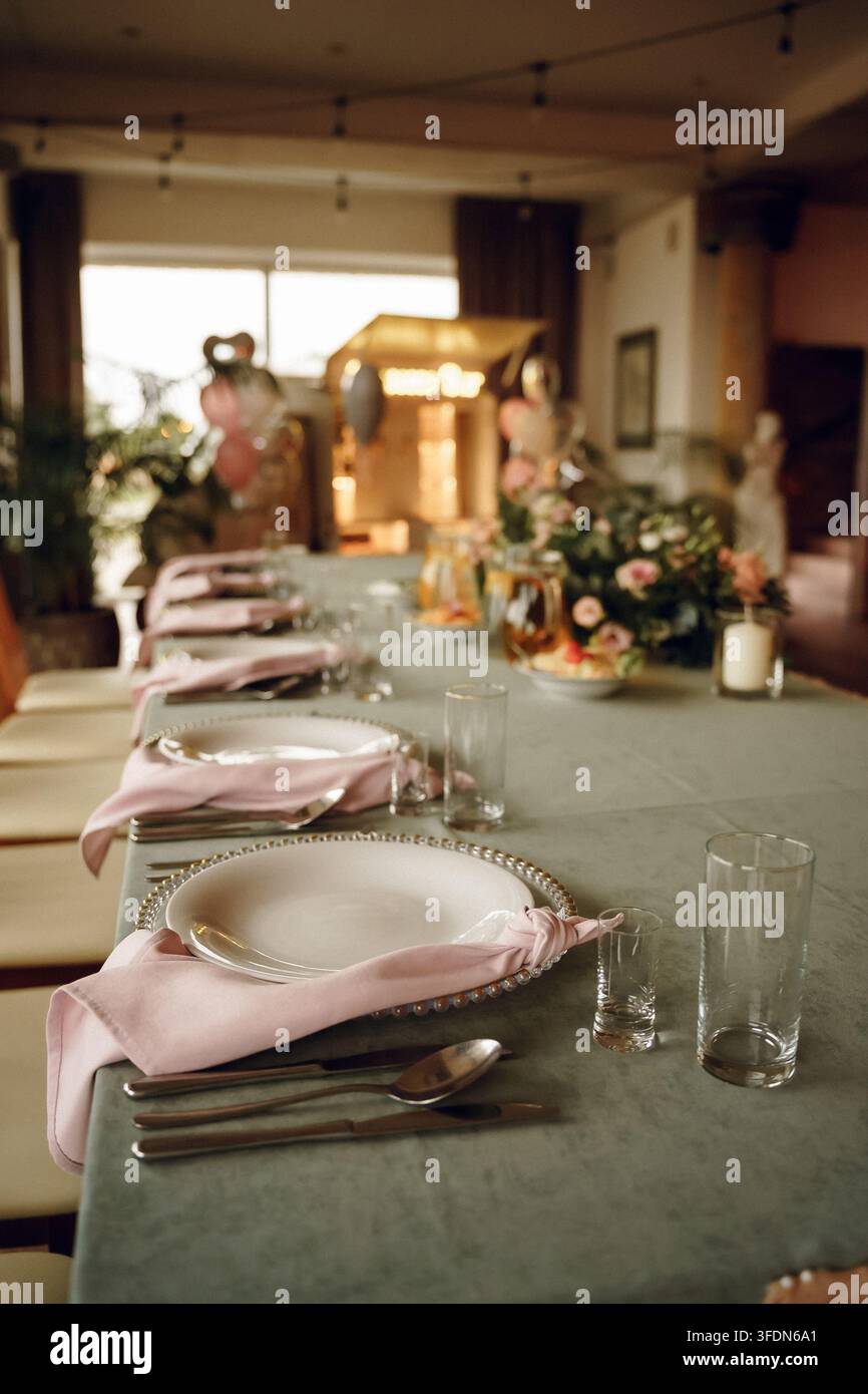 Tavolo da banchetto nuziale elegante con tovaglie di lino rosa polveroso, decorazioni floreali e illuminazione calda, perfetto per la pianificazione di eventi e temi di cucina di lusso Foto Stock