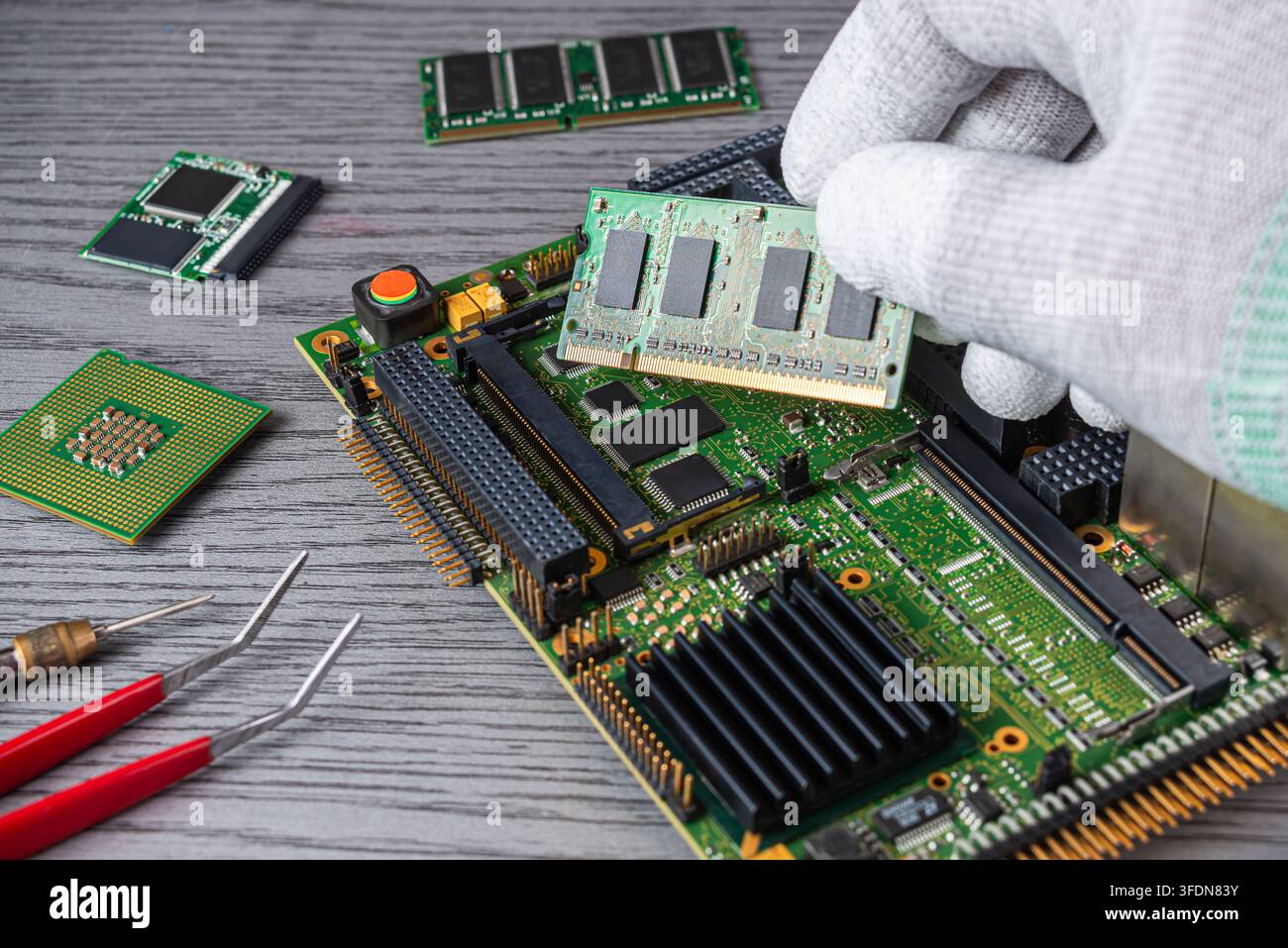 Si vede un tecnico che lavora su una scheda madre di un computer in un laboratorio. Maneggia con cura i chip di memoria e utilizza degli strumenti. Foto Stock