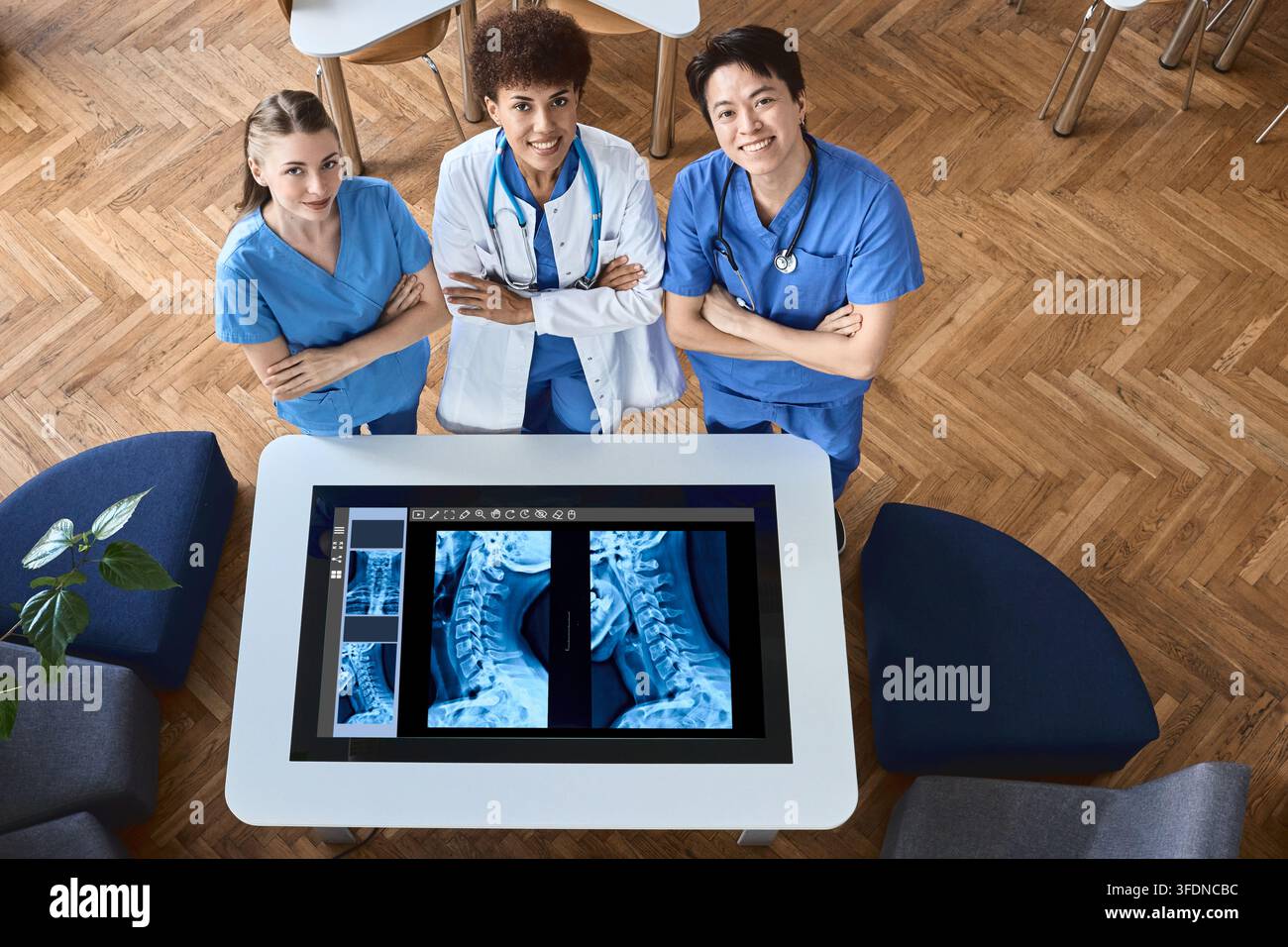 Ritratto aereo di un team clinico diversificato e sicuro di sé in piedi accanto a un tavolo di diagnostica digitale che visualizza radiografie delle vertebre cervicali Foto Stock
