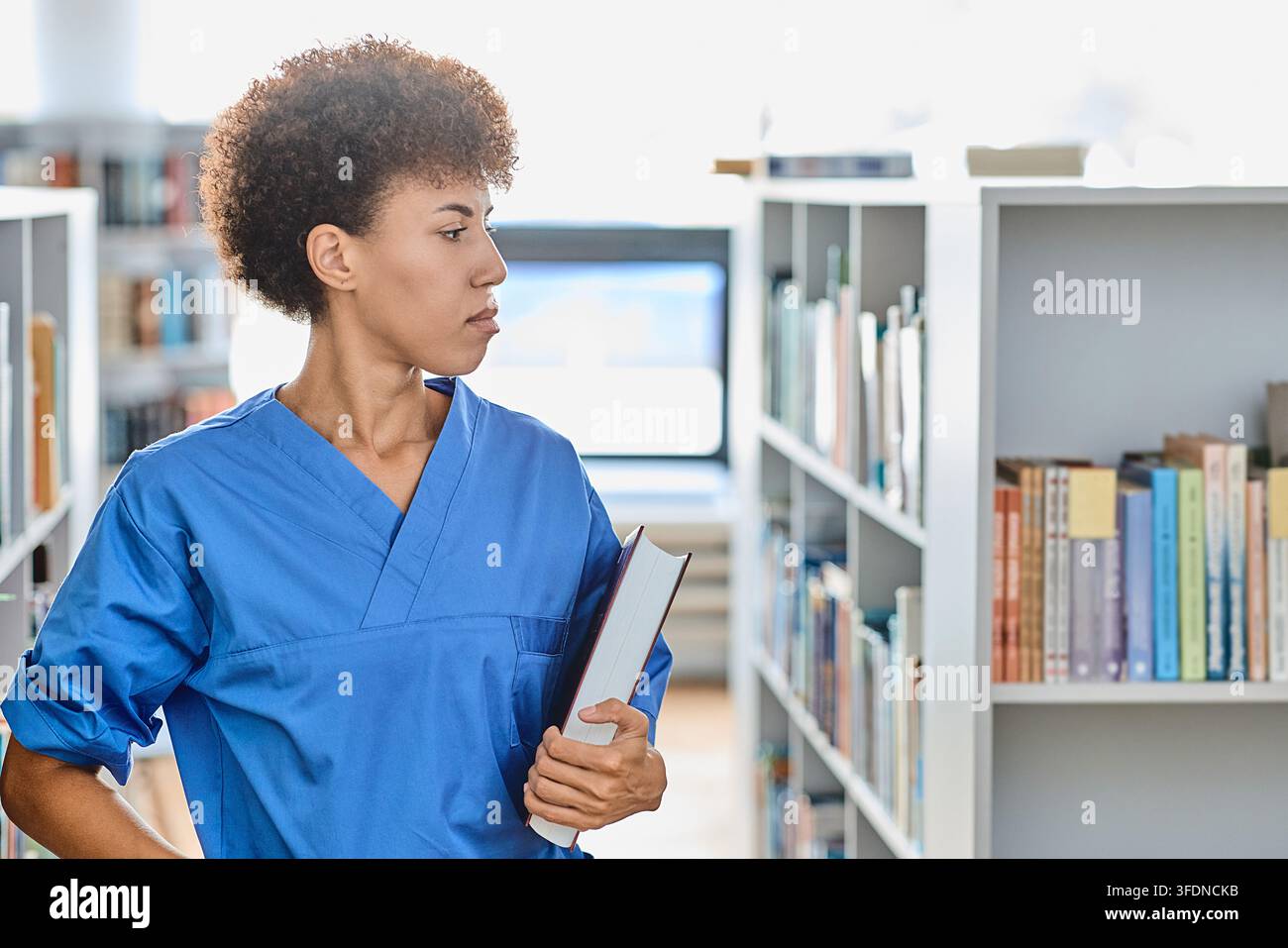 Catturare la profonda messa a fuoco e la dedizione intellettuale di un aspirante medico alla ricerca di conoscenza tra gli scaffali della biblioteca Foto Stock