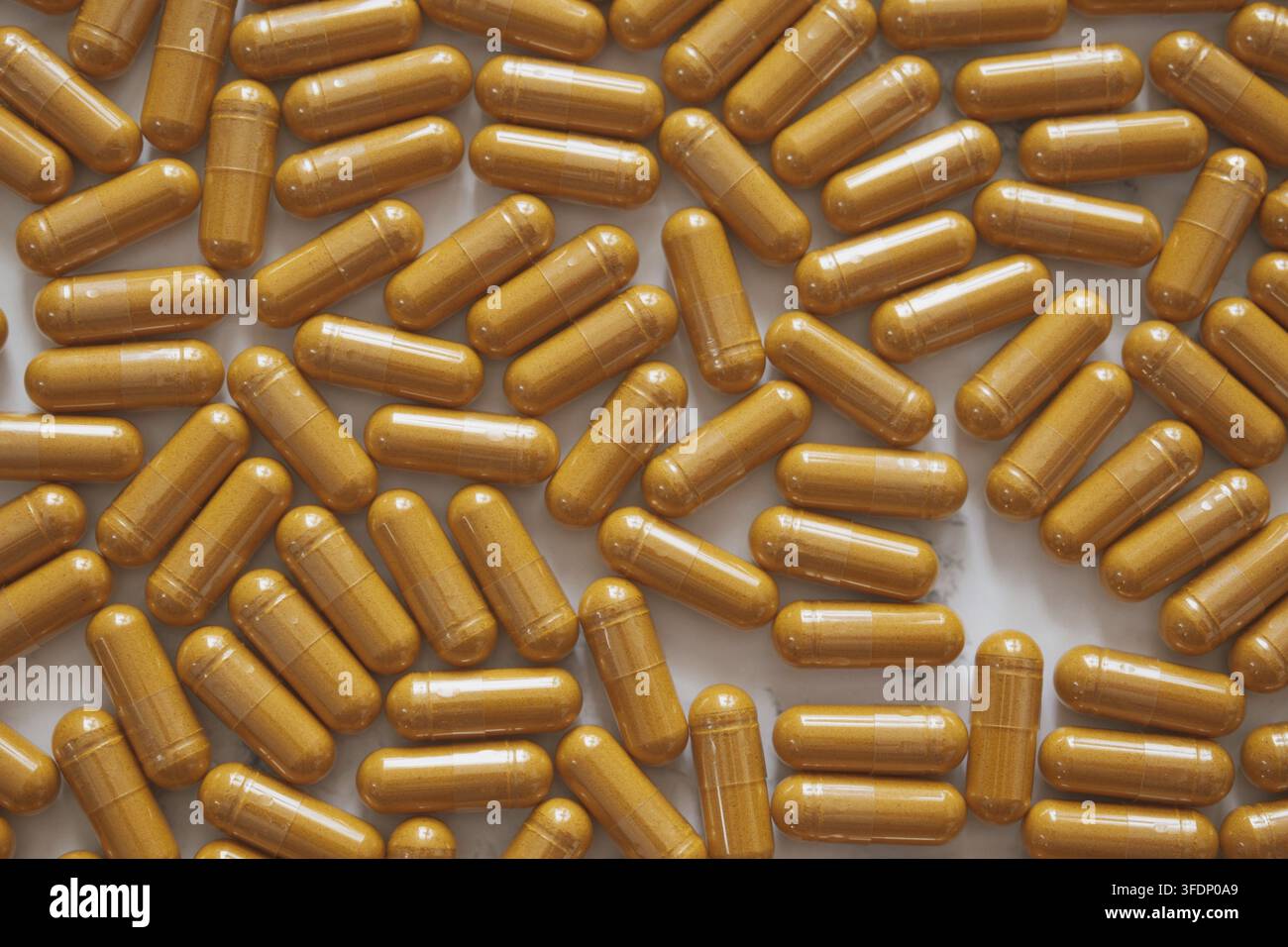 Piatto dall'alto minimalista con capsule luminose di curcumina sparse su marmo bianco, che mettono in risalto l'estetica vibrante del benessere e lo stile pulito e moderno Foto Stock