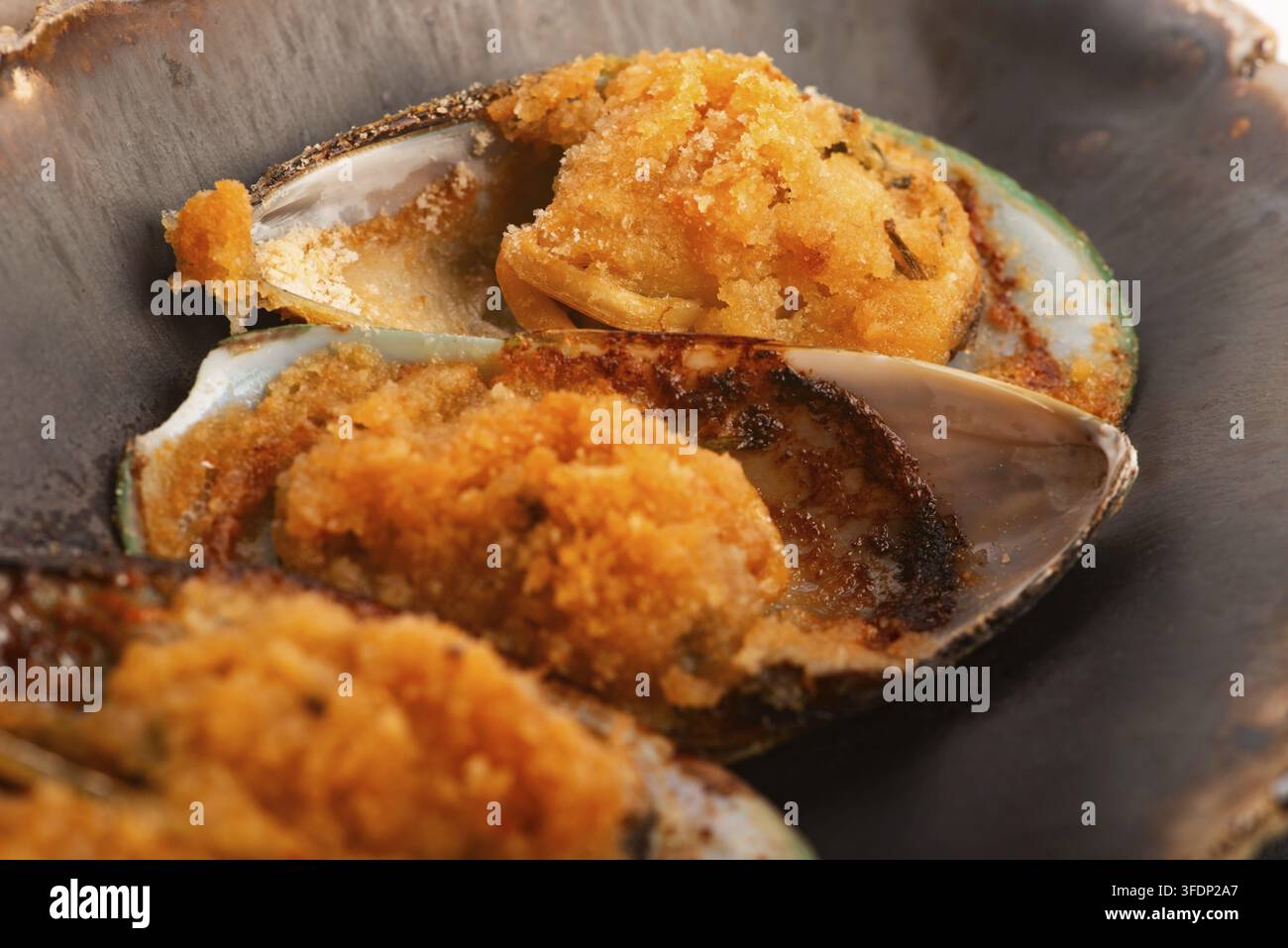Cozze neozelandesi cotte al forno con burro all'aglio e prezzemolo su un piatto di ceramica fatto a mano Foto Stock