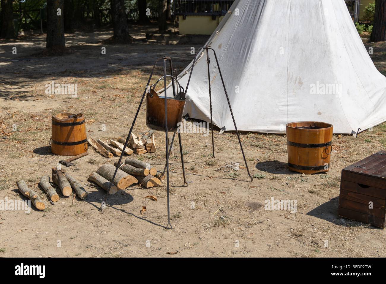 Allestimento da campeggio medievale con una pentola su treppiede, secchi di legno, legna da ardere e una tenda di tela all'aperto. Foto Stock