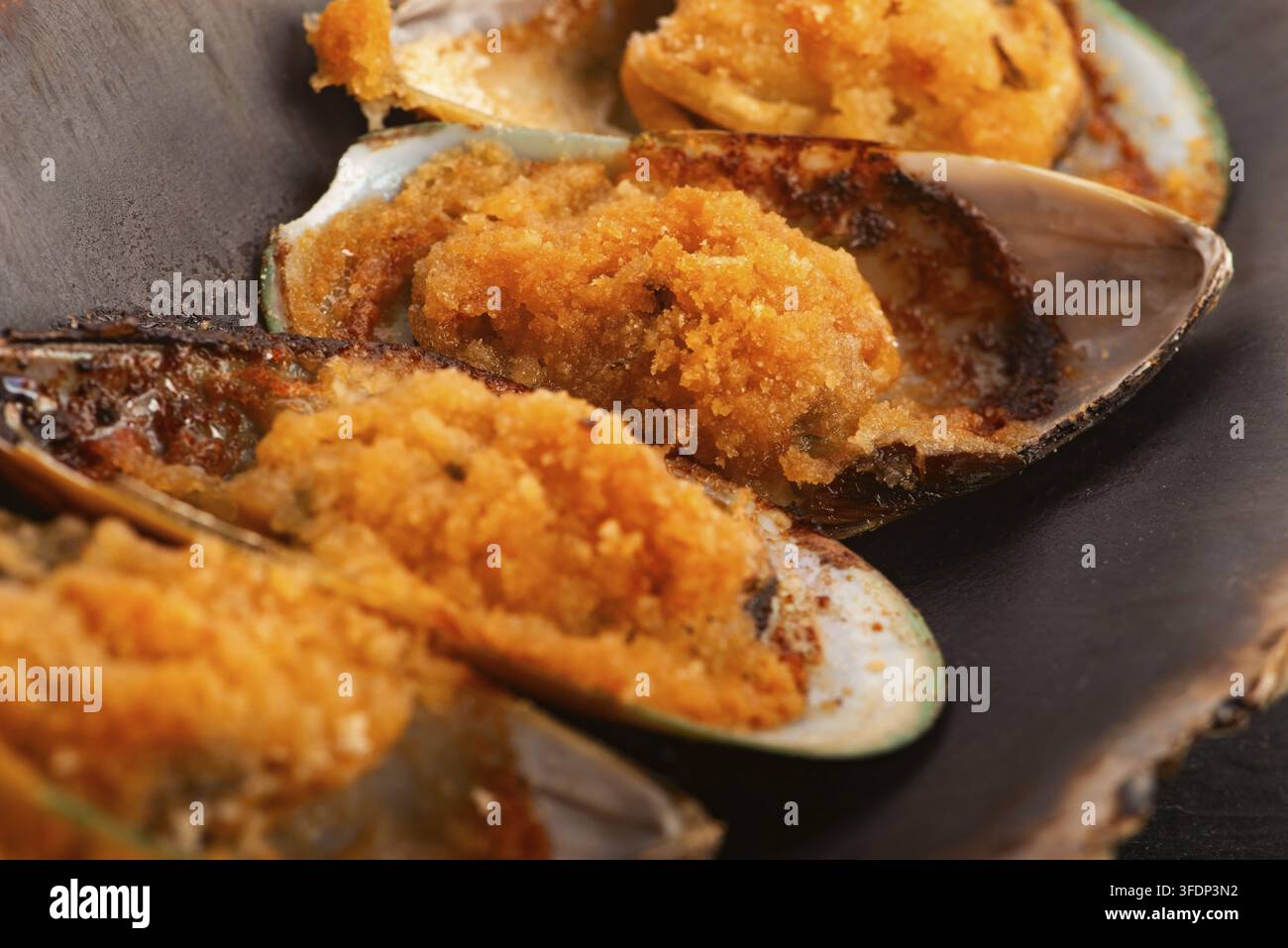 Cozze neozelandesi cotte al forno con burro all'aglio e prezzemolo su un piatto di ceramica fatto a mano Foto Stock