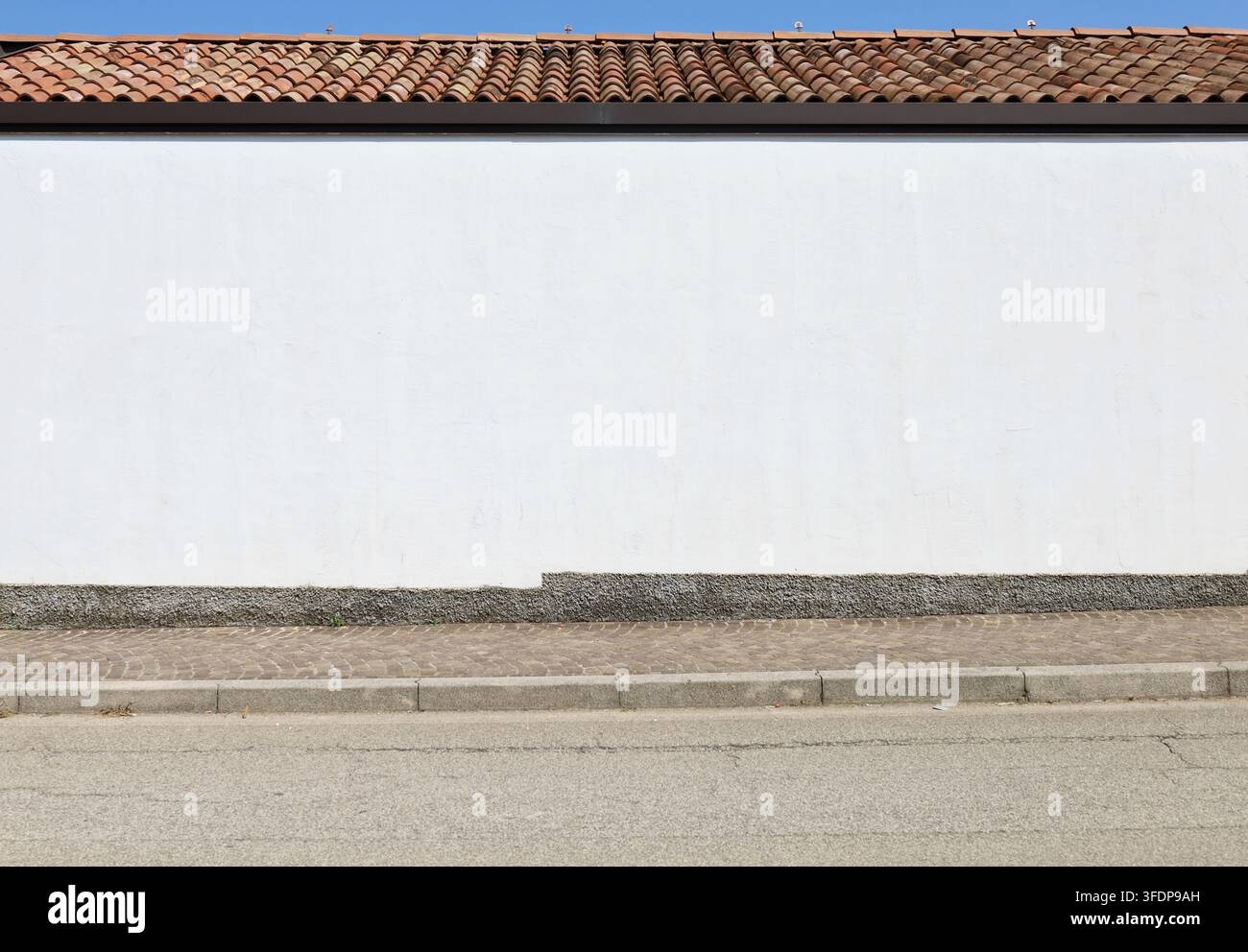 Facciata di casa in intonaco bianco sul lato della strada con tegole sul tetto. Cielo sopra, marciapiede e strada davanti. Sfondo per spazio di copia. Foto Stock