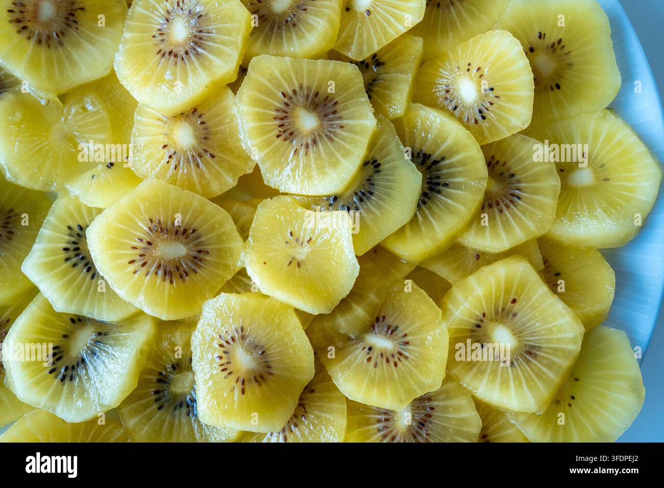 Primo piano luminoso di fette di kiwi dorate disposte su un piatto, che mostrano la polpa gialla succosa, i semini e la consistenza fresca. Spuntino o brea sano e vivace Foto Stock