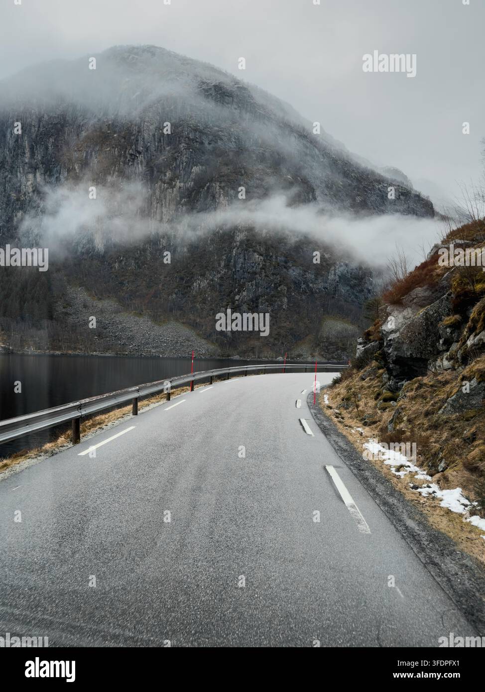 Una strada asfaltata si snoda con grazia tra una ripida parete rocciosa e un calmo fiordo in Norvegia. Foto Stock
