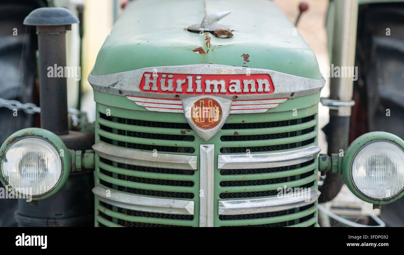 Primo piano della parte anteriore di un trattore verde Hürlimann vintage, che evidenzia la griglia cromata, i fari rotondi e la patina rugginosa invecchiata. Evoca l'eredità agricola, rurale Foto Stock