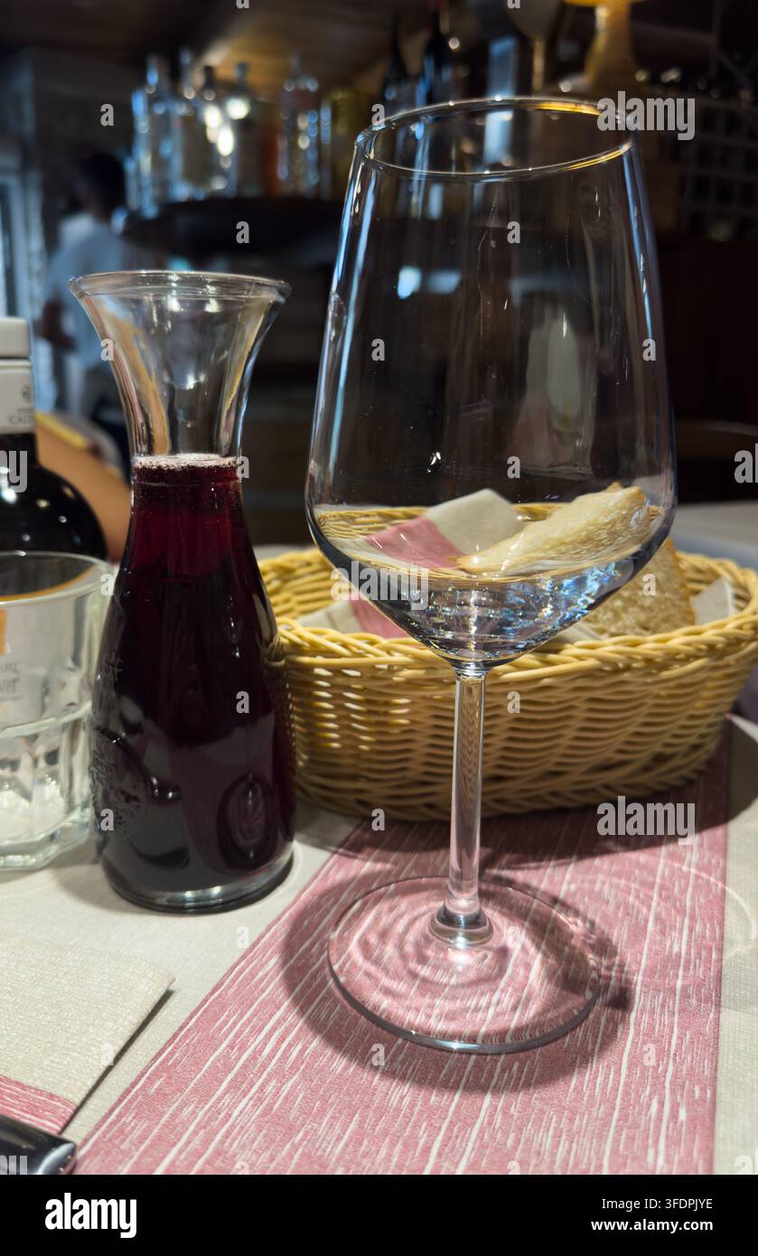 Un bicchiere da vino e una caraffa sono posizionati accanto al pane su un tavolo da ristorante con vino Vitis vinifera. La scena rappresenta la cena, l'ospitalità e il relax. Foto Stock