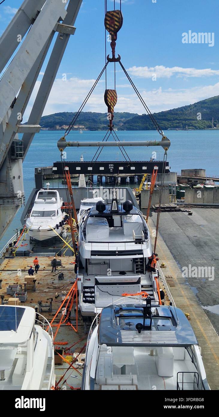 Grosso ponte portuale che carica yacht a motore di lusso sul ponte di una nave da carico in un terminal portuale industriale Foto Stock