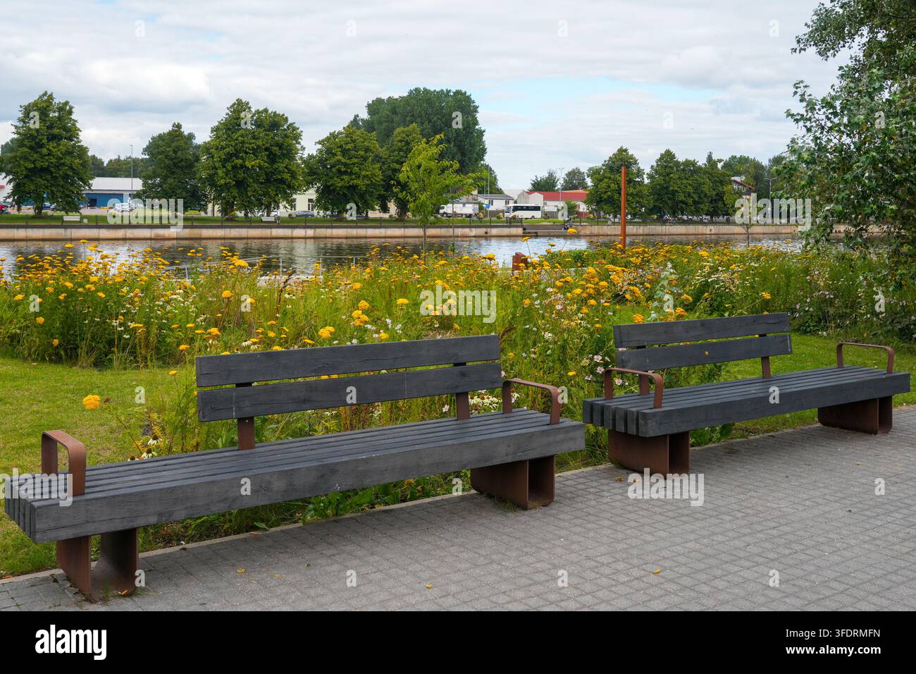 Verdure urbana e panchine sul fiume con prato di fiori selvatici a Liepaja, Lettonia Foto Stock