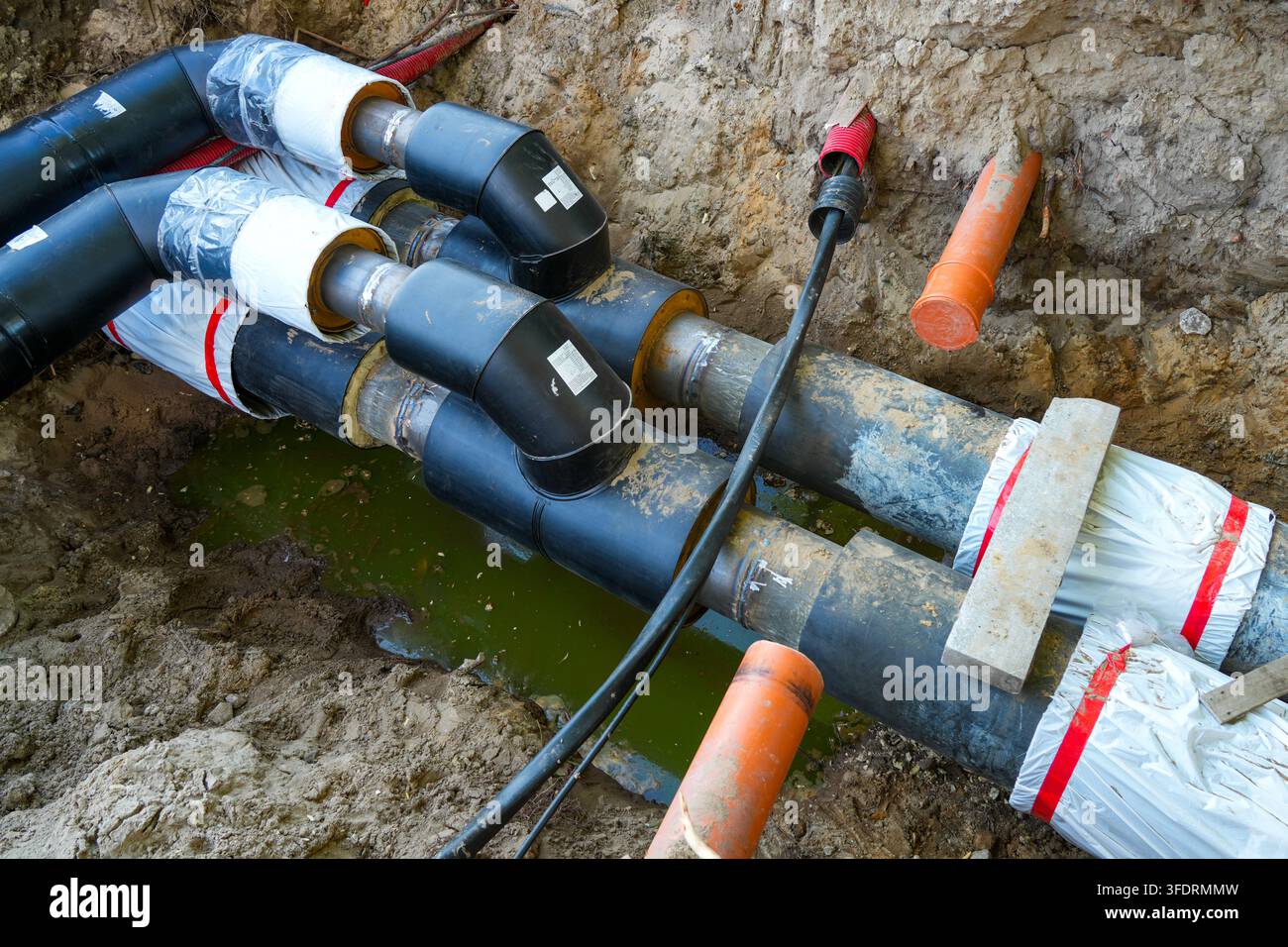 Tubi e gomiti di teleriscaldamento preisolati installati in una trincea sotterranea di utilità nel cantiere Foto Stock