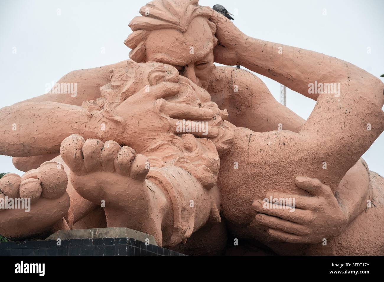 Primo piano di una scultura rosa massiccia che mostra due figure che si abbracciano e si baciano, evidenziando la superficie ruvida, le mani, i piedi e l'intimità emotiva in un Foto Stock