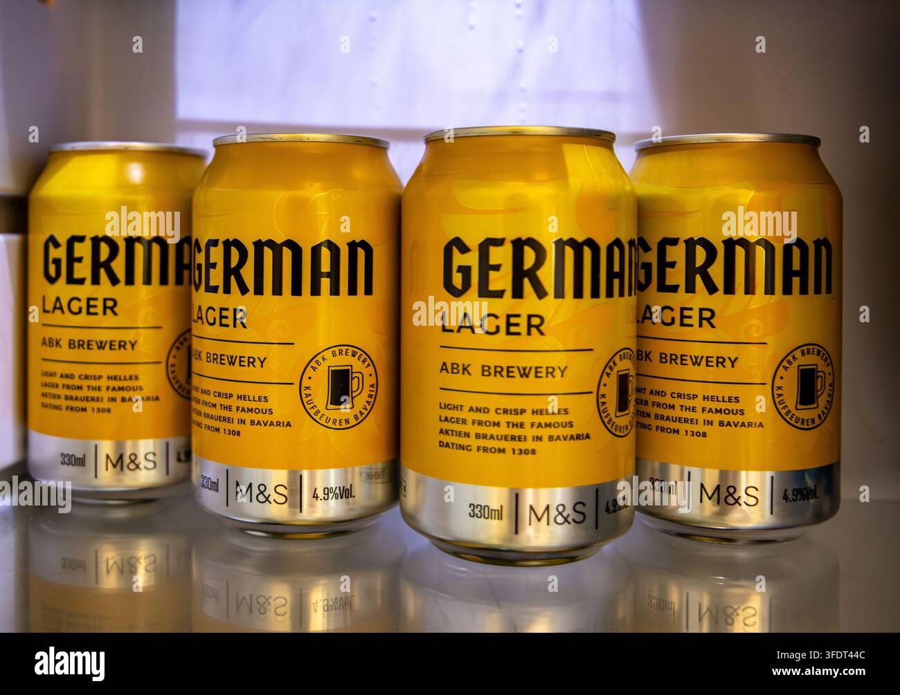 Lattine gialle di birra lager tedesca M&S in un frigorifero su uno scaffale riflettente Foto Stock
