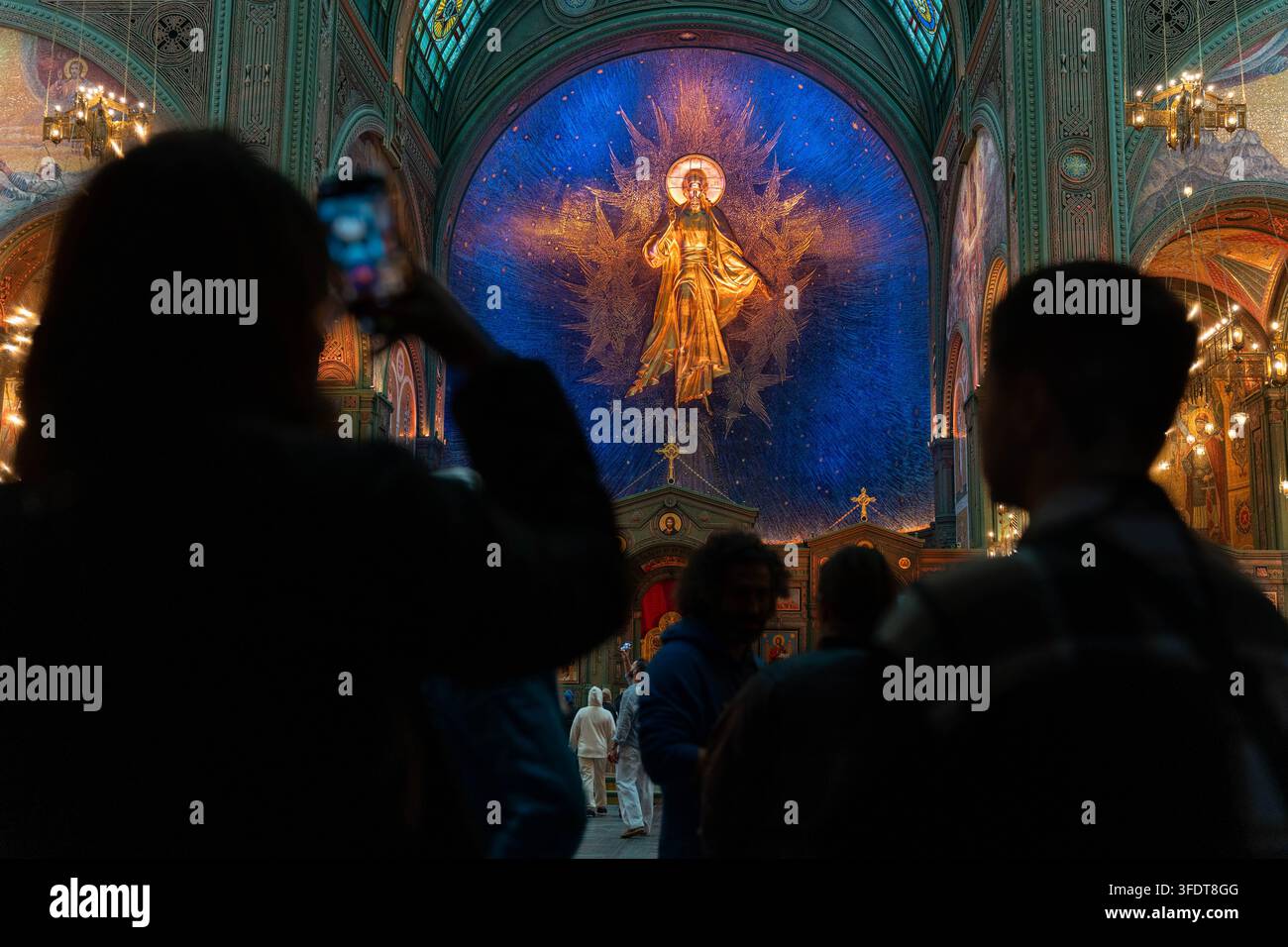 L'interno della cattedrale ortodossa si concentra su un mosaico radioso di Cristo. Le silouette scure dei visitatori in primo piano contrastano con le pareti blu impreziosite da gioielli Foto Stock