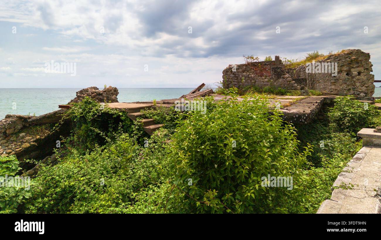 Una vista diurna di una struttura in pietra e cemento abbandonata e in rovina situata direttamente su una costa. L'edificio fatiscente presenta pietra sgretolante Foto Stock
