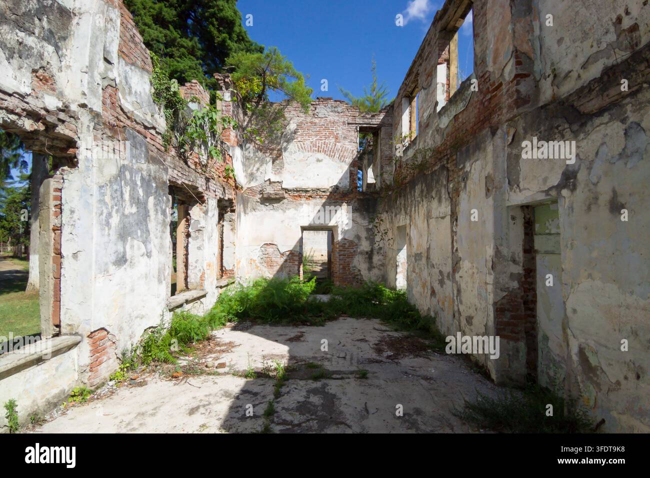Una vista diurna dell'interno di una rovina di edificio abbandonato e senza tetto. La struttura presenta muri sgretolati con mattoni rossi esposti e vernice bianca s Foto Stock