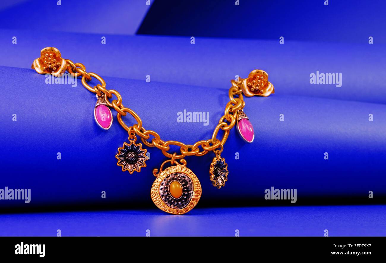 Collana con ciondoli in tonalità dorate con pendenti floreali e circolari e accenti rosa, esposta su uno sfondo blu vivace. Foto Stock