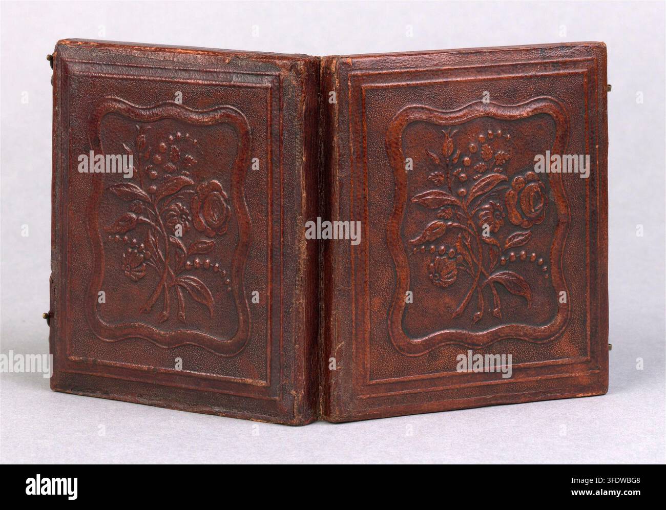 Un giovane uomo seduto con il braccio sinistro su un tavolo, in una fotografia del XIX secolo, specificamente tra il 1842 e il 1855, con un libro o astuccio rilegato in pelle marrone scuro aperto per mostrare due pannelli rettangolari identici con disegni floreali in rilievo. Foto Stock