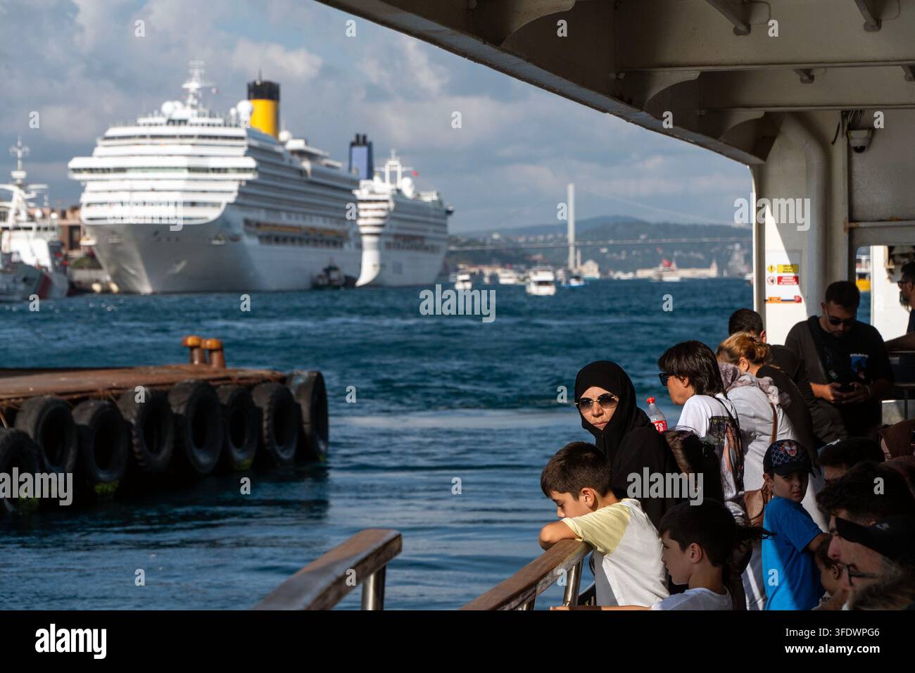 Un gruppo di persone si trova sul ponte di una nave e osserva grandi navi da crociera ormeggiate nel porto. Foto Stock