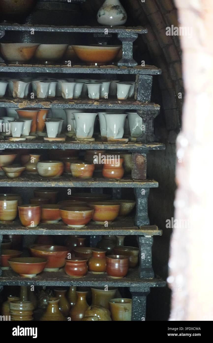 File di ciotole e tazze in ceramica smaltata colorata impilate su scaffali di legno a Jingdezhen, Cina Foto Stock