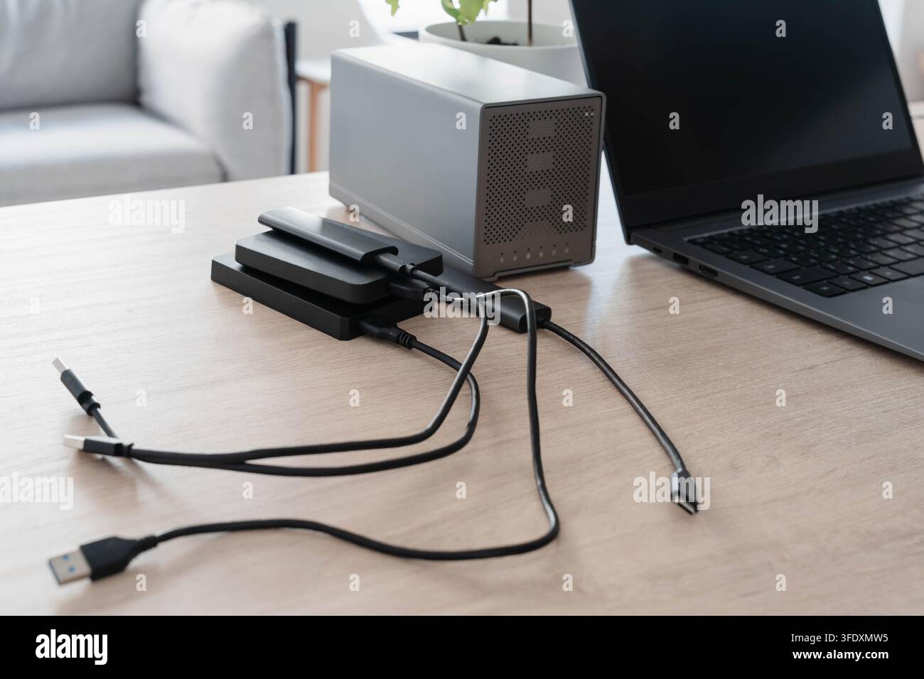 Pila di dischi rigidi esterni portatili e un involucro RAID a due bay collegati tramite cavi USB a un laptop su una scrivania di legno. Backup dei dati e ridondanza Foto Stock