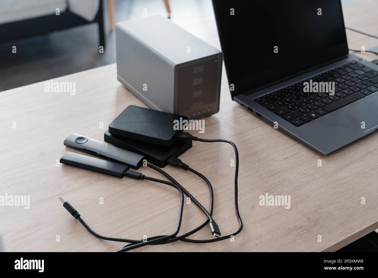 Unità esterne, un contenitore di archiviazione di rete e un hub USB sono collegati tramite cavo a un laptop aperto su una scrivania di legno. Backup dei dati e sincronizzazione dello spazio di archiviazione cloud in Foto Stock