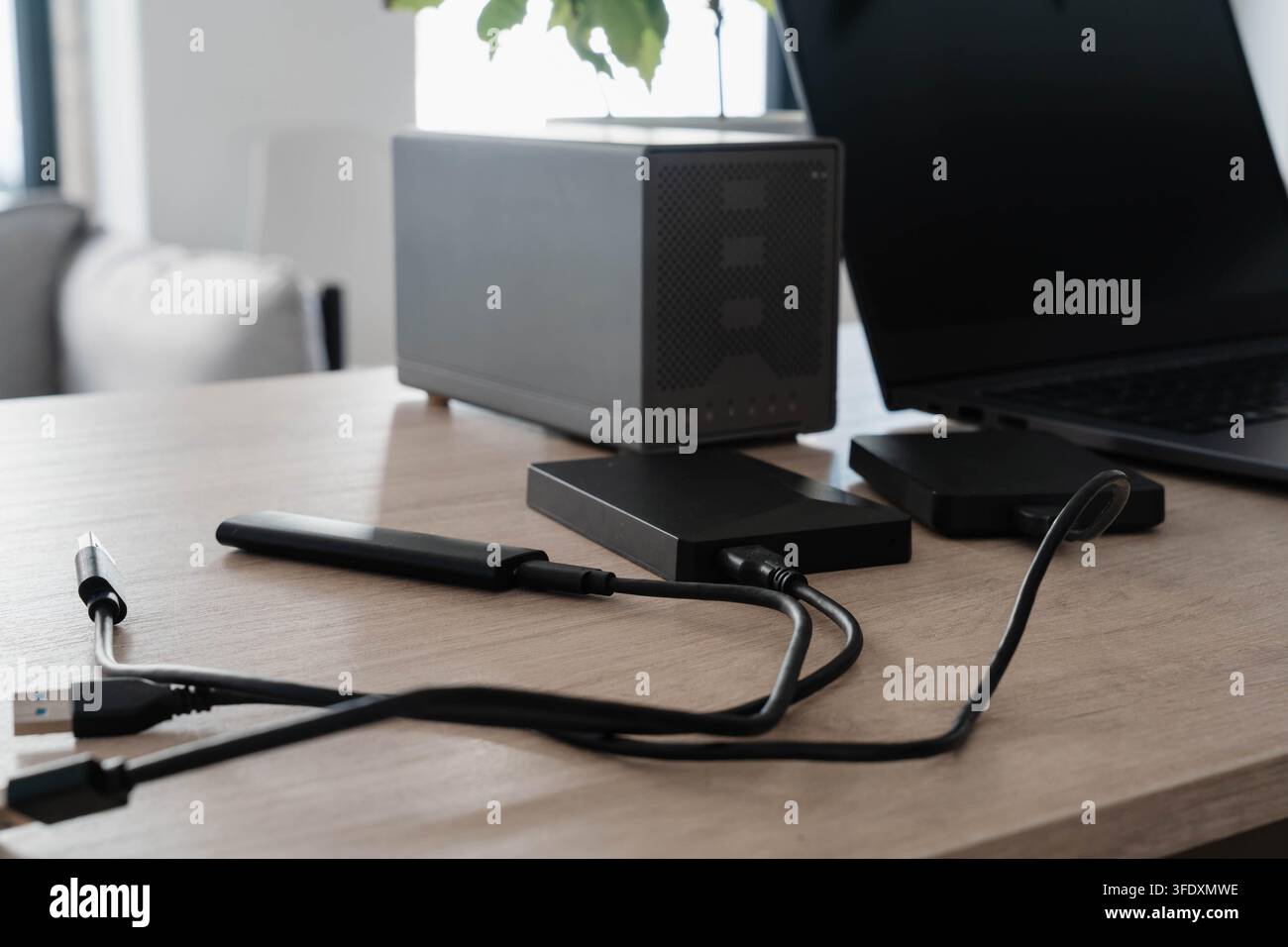 Dischi rigidi esterni, un SSD portatile e cavi USB collegati a un laptop su una scrivania di legno. Configurazione dell’ufficio domestico per il backup dei dati, l’archiviazione dei file e la sicurezza Foto Stock