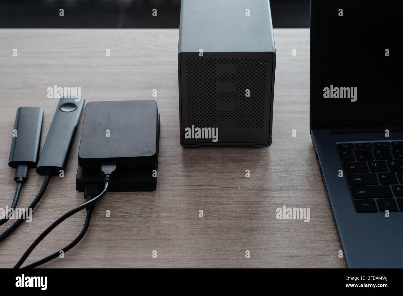 Dischi rigidi esterni portatili e alloggi SSD collegati tramite cavi a un laptop su una scrivania di legno. Archiviazione dei dati e flusso di lavoro di backup per fotografi Foto Stock