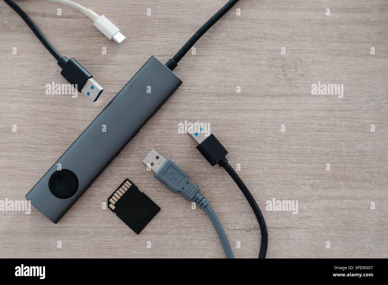 Hub USB in alluminio con indicatore luminoso giace su una scrivania di legno accanto a cavi di collegamento e una scheda di memoria. Connettività periferica e trasferimento di dati Foto Stock