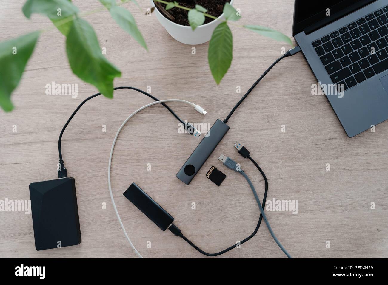 Hub USB collegato a un laptop su una scrivania di legno con un disco rigido esterno, un SSD portatile, una scheda di memoria e cavi scollegati intorno. Porte espandibili Foto Stock