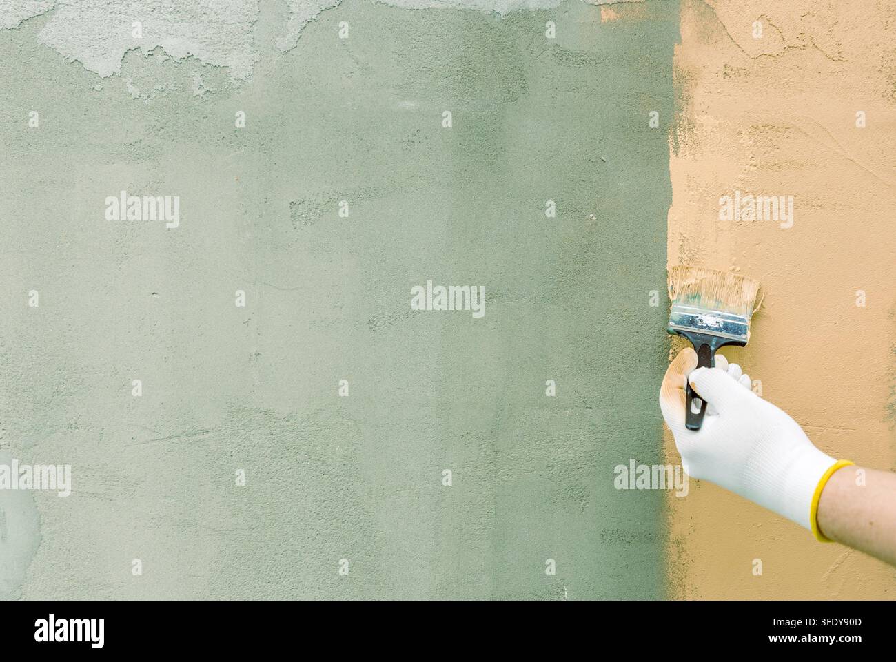 Mano dipinge il muro con pennello e guanto bianco. Il muro si divide tra texture verdi e marroni Foto Stock