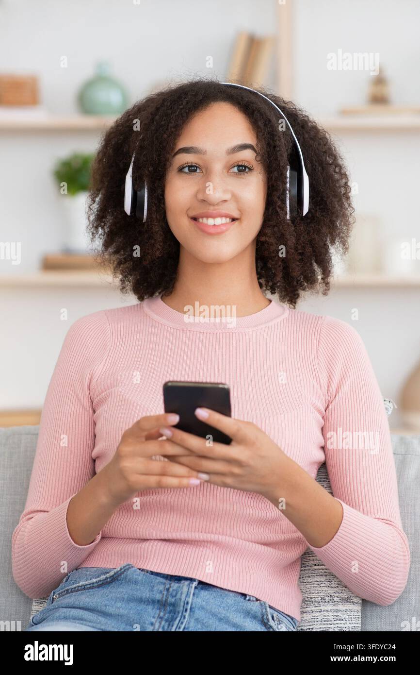 Felice giovane afroamericana femmina in cuffia wireless tenere telefono Foto Stock